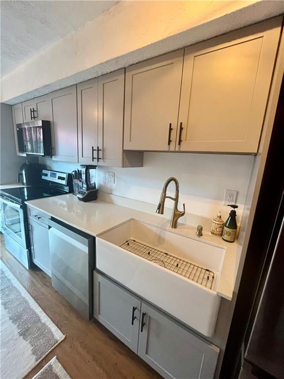 kitchen with a sink, stainless steel appliances, wood finished floors, and light countertops