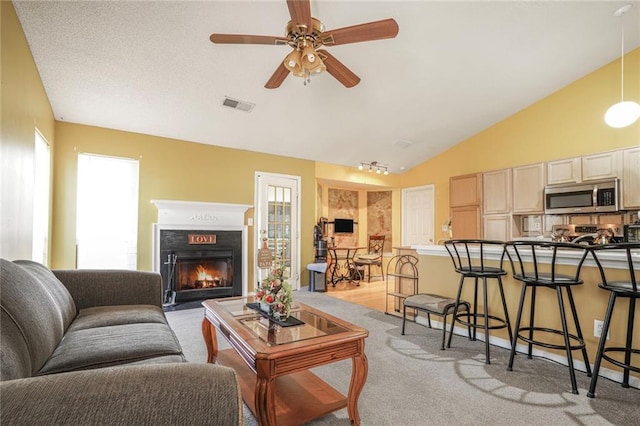 living room with a warm lit fireplace, visible vents, a ceiling fan, light colored carpet, and lofted ceiling