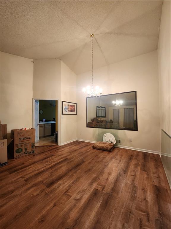 unfurnished living room featuring a textured ceiling, an inviting chandelier, high vaulted ceiling, and wood-type flooring