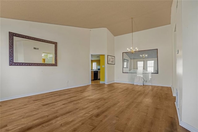 unfurnished living room featuring baseboards, high vaulted ceiling, wood finished floors, and an inviting chandelier