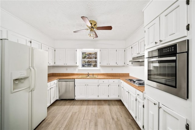 kitchen featuring light wood-style flooring, light countertops, under cabinet range hood, appliances with stainless steel finishes, and white cabinetry