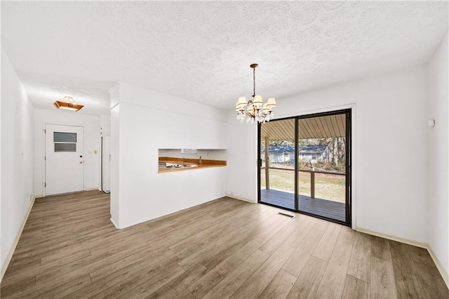 unfurnished dining area with visible vents, a notable chandelier, wood finished floors, and a textured ceiling