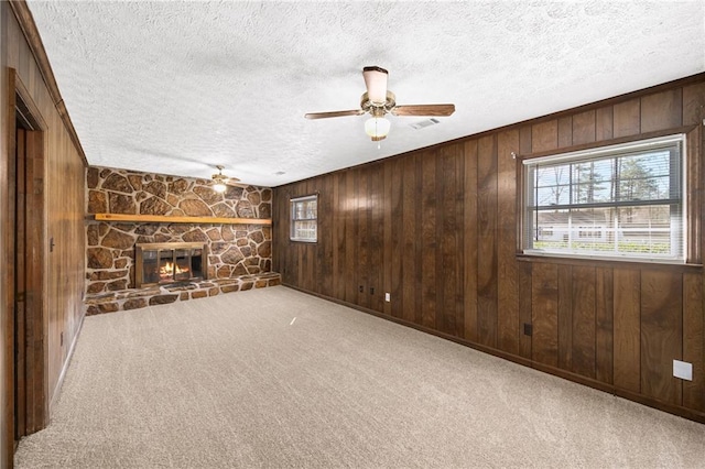 unfurnished living room with a fireplace, wooden walls, carpet, and a textured ceiling