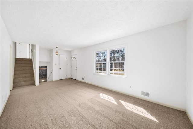 unfurnished living room featuring visible vents, stairs, carpet flooring, a fireplace, and a textured ceiling