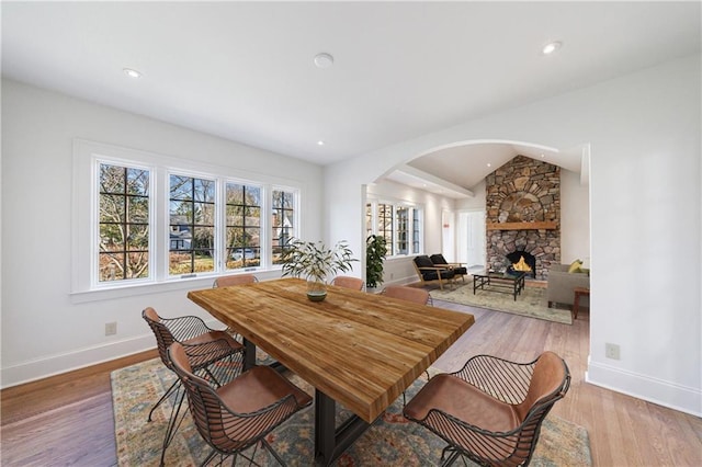 dining area with a fireplace, light hardwood / wood-style flooring, and lofted ceiling