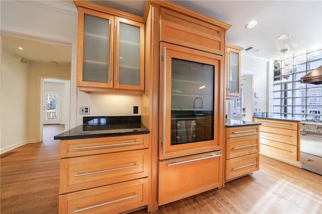 kitchen with dark stone countertops, crown molding, light hardwood / wood-style flooring, and exhaust hood