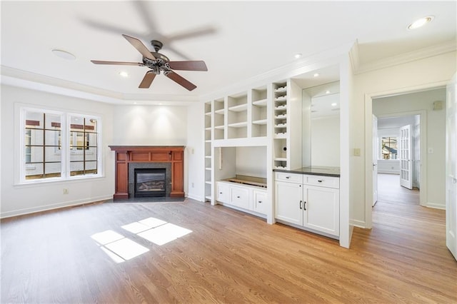 unfurnished living room featuring ceiling fan, built in features, crown molding, and light hardwood / wood-style flooring