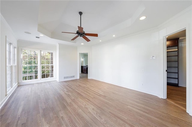 unfurnished living room featuring a raised ceiling, ceiling fan, light wood-type flooring, and ornamental molding