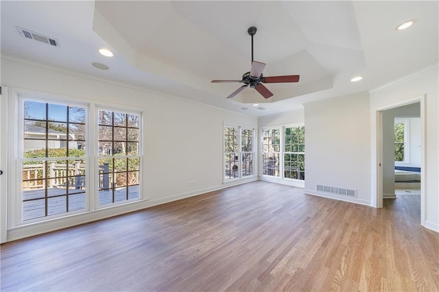 unfurnished room featuring a raised ceiling, ceiling fan, light hardwood / wood-style flooring, and crown molding