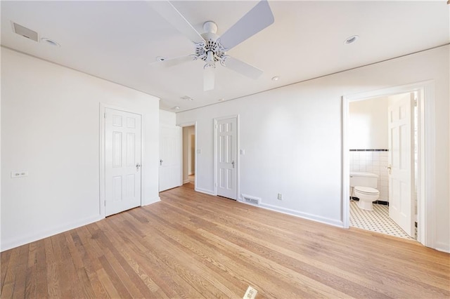 unfurnished bedroom featuring connected bathroom, ceiling fan, tile walls, and light wood-type flooring