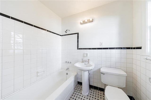 bathroom featuring tile patterned flooring, tiled shower / bath, tile walls, and toilet