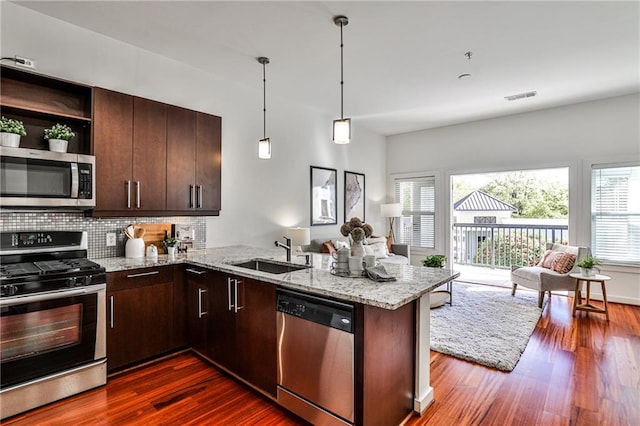 kitchen with stainless steel appliances, sink, kitchen peninsula, light stone countertops, and dark wood-type flooring