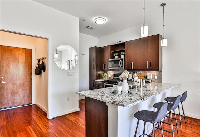 kitchen with decorative light fixtures, a kitchen bar, backsplash, appliances with stainless steel finishes, and dark brown cabinetry