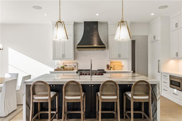 kitchen with stainless steel microwave, an island with sink, and wall chimney exhaust hood