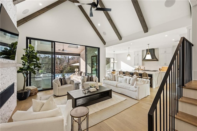 living area with ceiling fan, high vaulted ceiling, light wood-style flooring, a fireplace, and beamed ceiling