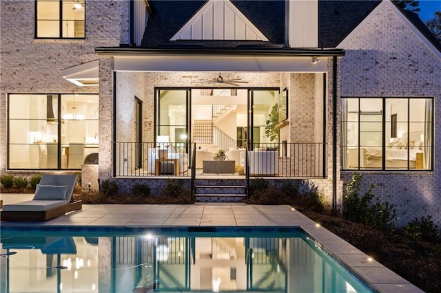 back of house featuring board and batten siding, brick siding, an outdoor pool, and a patio