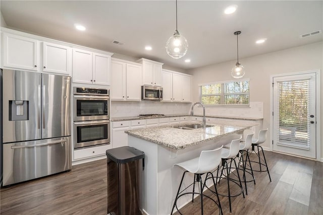 kitchen with a sink, tasteful backsplash, white cabinetry, dark wood-type flooring, and appliances with stainless steel finishes