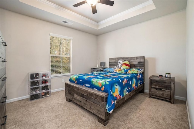carpeted bedroom featuring a ceiling fan, a tray ceiling, baseboards, ornamental molding, and visible vents