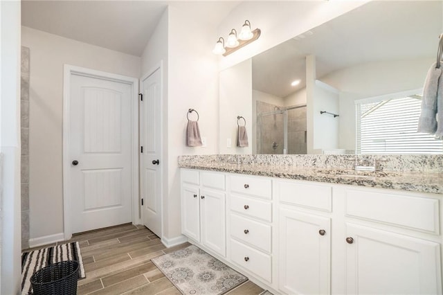 full bath featuring wood tiled floor, double vanity, a sink, baseboards, and a stall shower