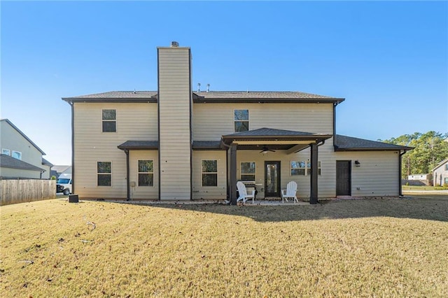 rear view of property featuring a chimney, fence, ceiling fan, a patio, and a lawn