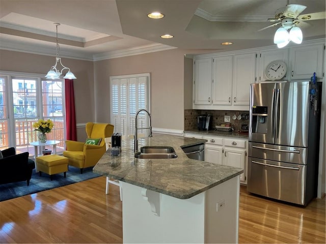 kitchen with a sink, light wood-style floors, appliances with stainless steel finishes, white cabinetry, and a raised ceiling