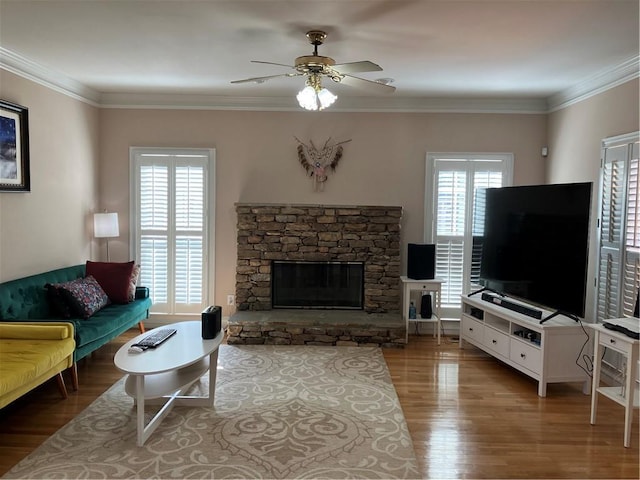 living room with a stone fireplace, crown molding, ceiling fan, and wood finished floors