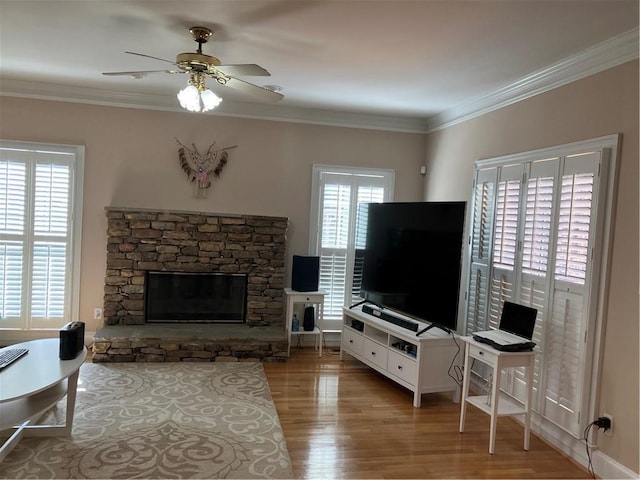 living room featuring a stone fireplace, crown molding, wood finished floors, and ceiling fan