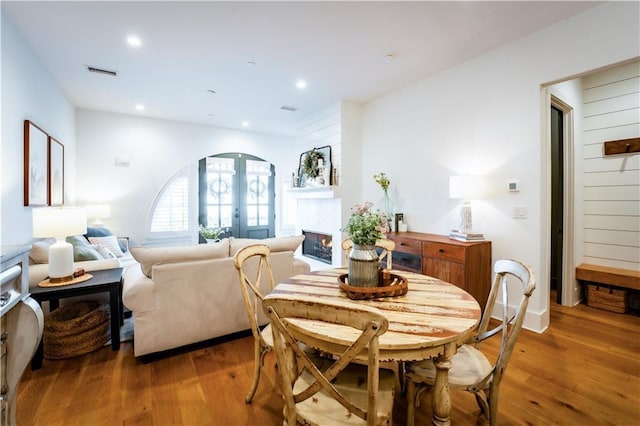 dining space featuring recessed lighting, visible vents, a warm lit fireplace, and wood finished floors