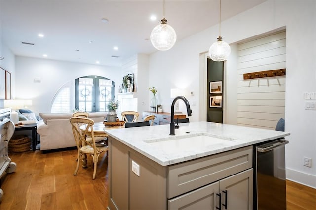 kitchen with light wood-style flooring, a sink, stainless steel dishwasher, open floor plan, and hanging light fixtures