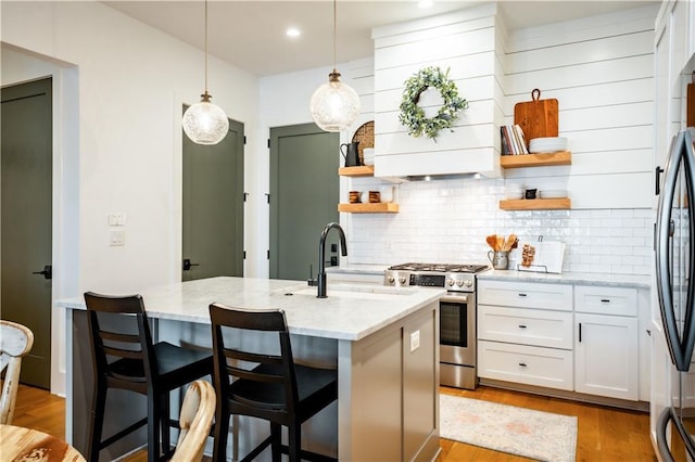 kitchen featuring a sink, open shelves, light stone counters, appliances with stainless steel finishes, and decorative backsplash