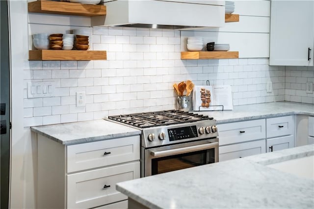 kitchen featuring backsplash, stainless steel gas range, wall chimney exhaust hood, and open shelves