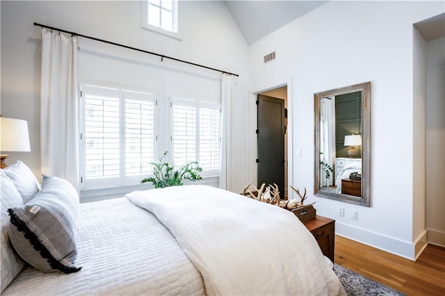 bedroom with visible vents, high vaulted ceiling, access to outside, wood finished floors, and baseboards