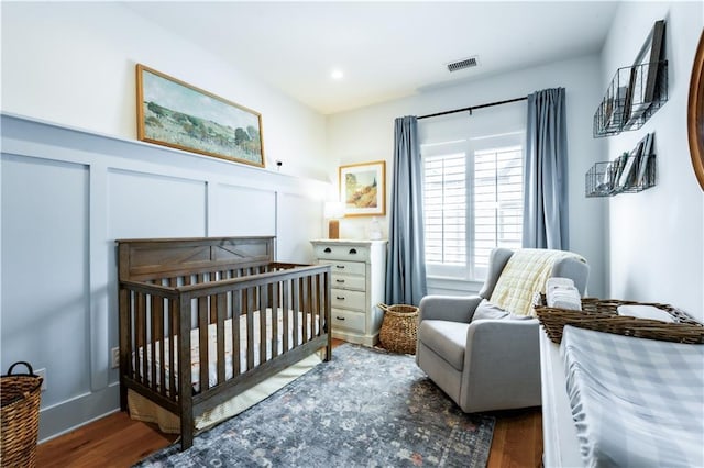 bedroom with a decorative wall, a nursery area, wood finished floors, and visible vents