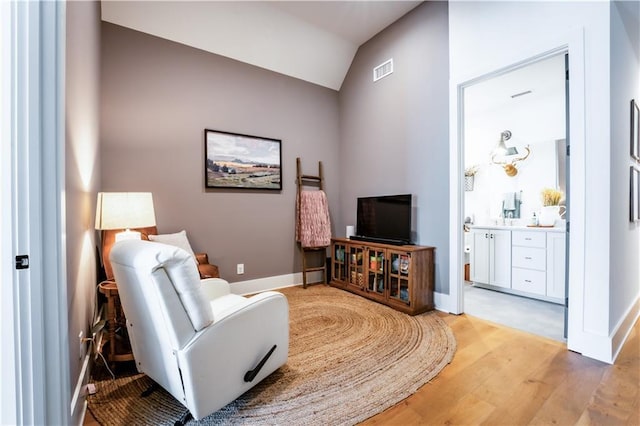 sitting room featuring visible vents, baseboards, light wood-style flooring, and vaulted ceiling