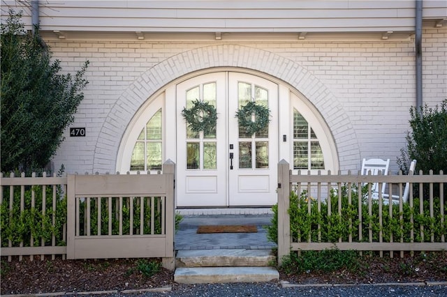 view of exterior entry featuring brick siding and fence