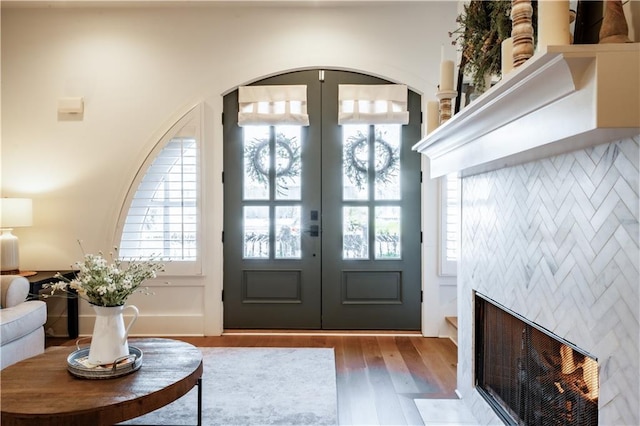 foyer with french doors, a fireplace with flush hearth, arched walkways, and wood finished floors