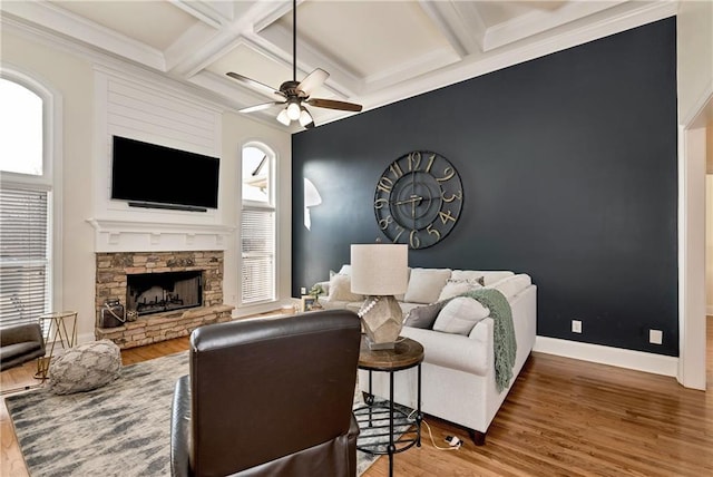 living room featuring coffered ceiling, a stone fireplace, ceiling fan, beam ceiling, and hardwood / wood-style floors