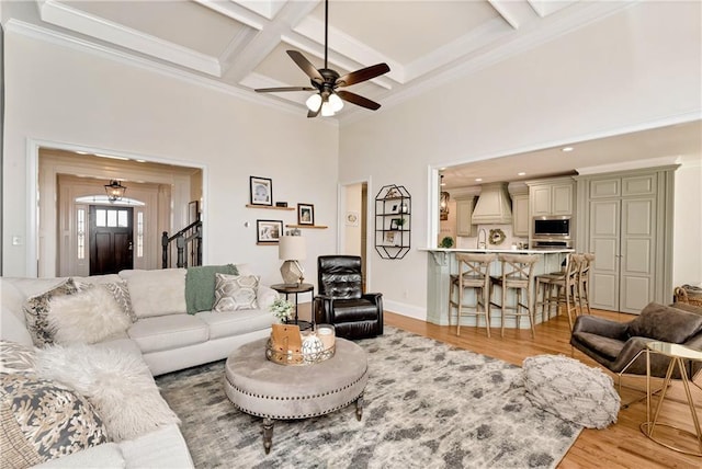 living room featuring crown molding, beam ceiling, a towering ceiling, coffered ceiling, and light hardwood / wood-style floors