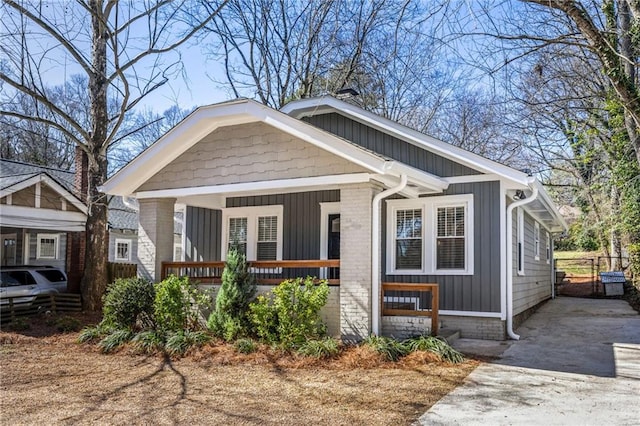 bungalow-style house featuring a porch, brick siding, driveway, and board and batten siding