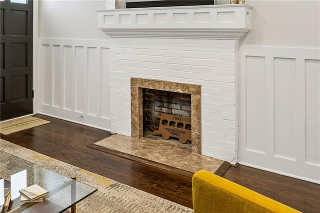 room details featuring a fireplace with raised hearth, wainscoting, and wood finished floors