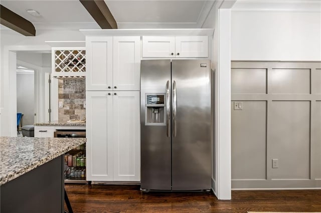 kitchen with light stone counters, a decorative wall, white cabinets, stainless steel fridge, and beamed ceiling