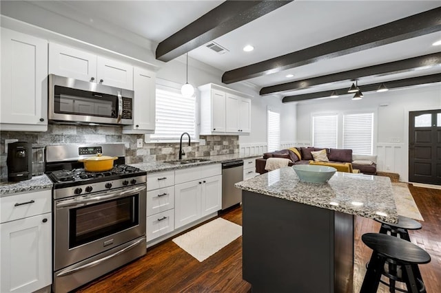 kitchen featuring stainless steel appliances, open floor plan, white cabinetry, a sink, and a kitchen island