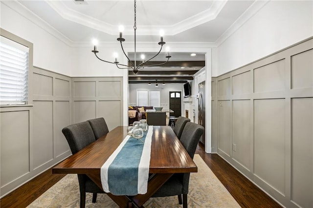 dining space featuring crown molding, a decorative wall, dark wood-type flooring, and a raised ceiling