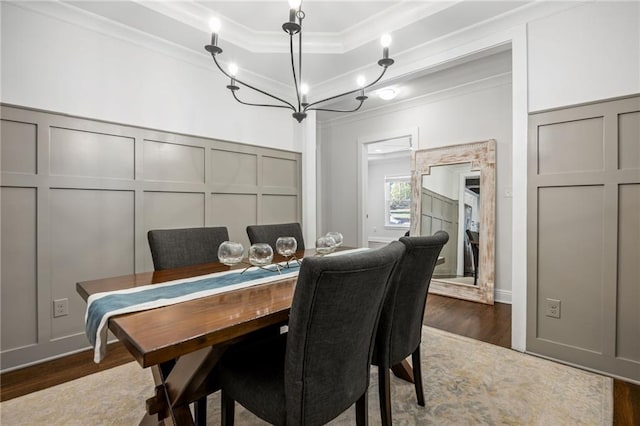 dining area featuring dark wood-type flooring, a tray ceiling, crown molding, and a decorative wall