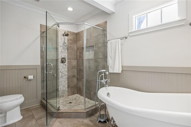 bathroom featuring toilet, a wainscoted wall, tile patterned floors, a freestanding tub, and a shower stall