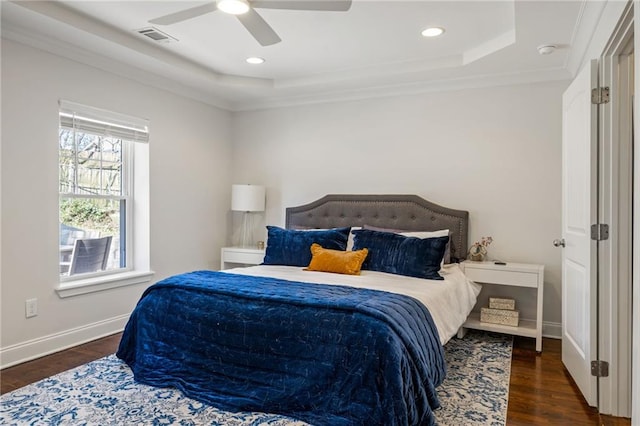 bedroom with a tray ceiling, dark wood-style flooring, visible vents, and baseboards