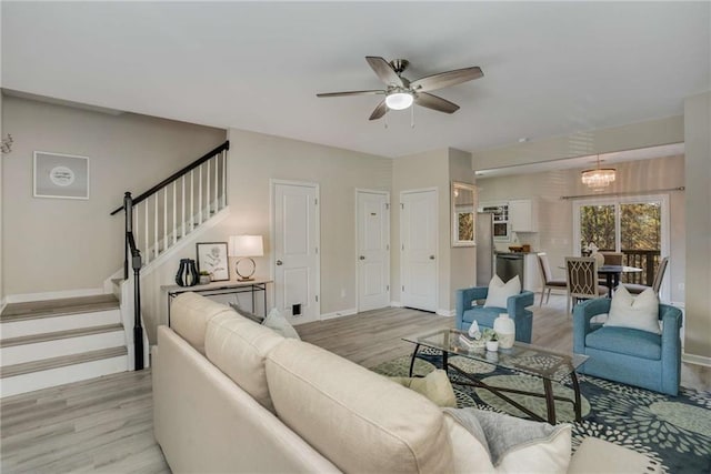 living area with ceiling fan with notable chandelier, light wood-style flooring, baseboards, and stairs