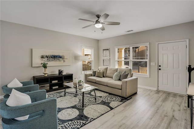 living room with baseboards, light wood-style flooring, visible vents, and a ceiling fan