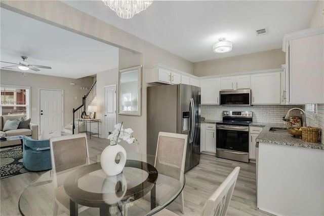 dining space featuring light wood-style flooring, stairs, visible vents, and ceiling fan with notable chandelier