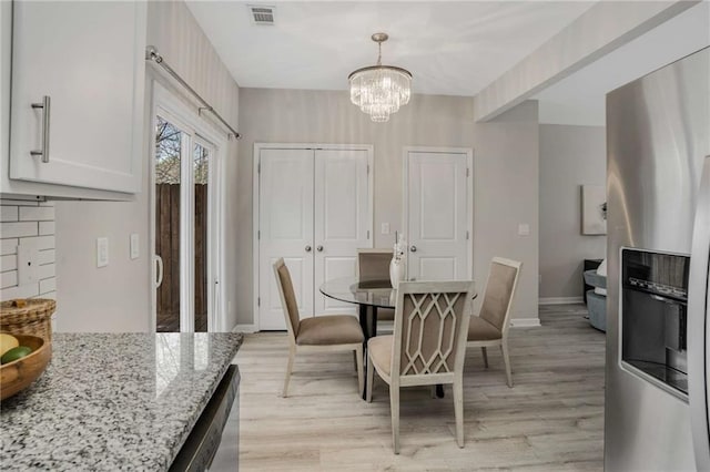 dining room featuring light wood finished floors, baseboards, visible vents, and an inviting chandelier